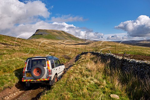 Car on unsurfaced road near Helwith Bridge with Pen y Ghent beyond Yorkshire Dales National Park England